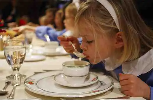 A young, blonde girl sipping on soup.