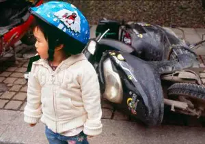 A little Chinese girl standing in front of a broken motorcycle 