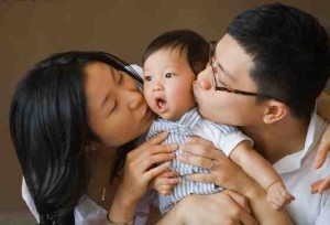 Two parents kissing their baby on the cheeks