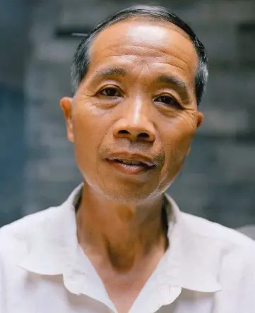 A Chinese man stares into a camera, not smiling.