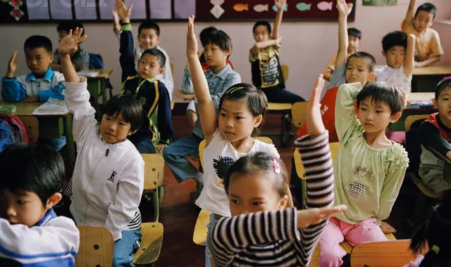 Young students in China raise their hands in the classroom.